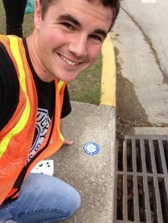 A volunteer posing next to marked storm drain.